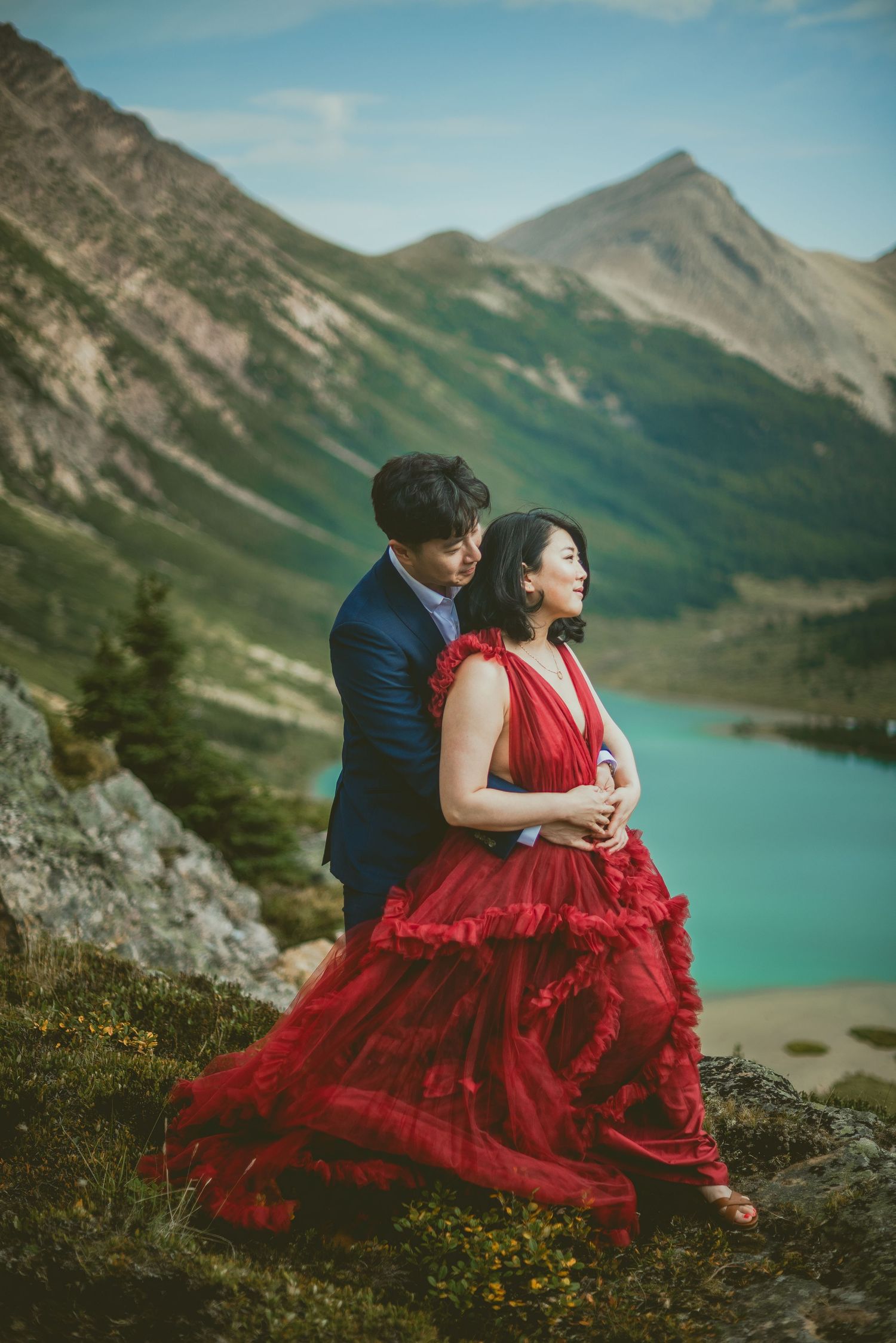 A couple in formal attire poses against a stunning mountain backdrop with turquoise lake views. Alberta Helicopter Elopement Photographer