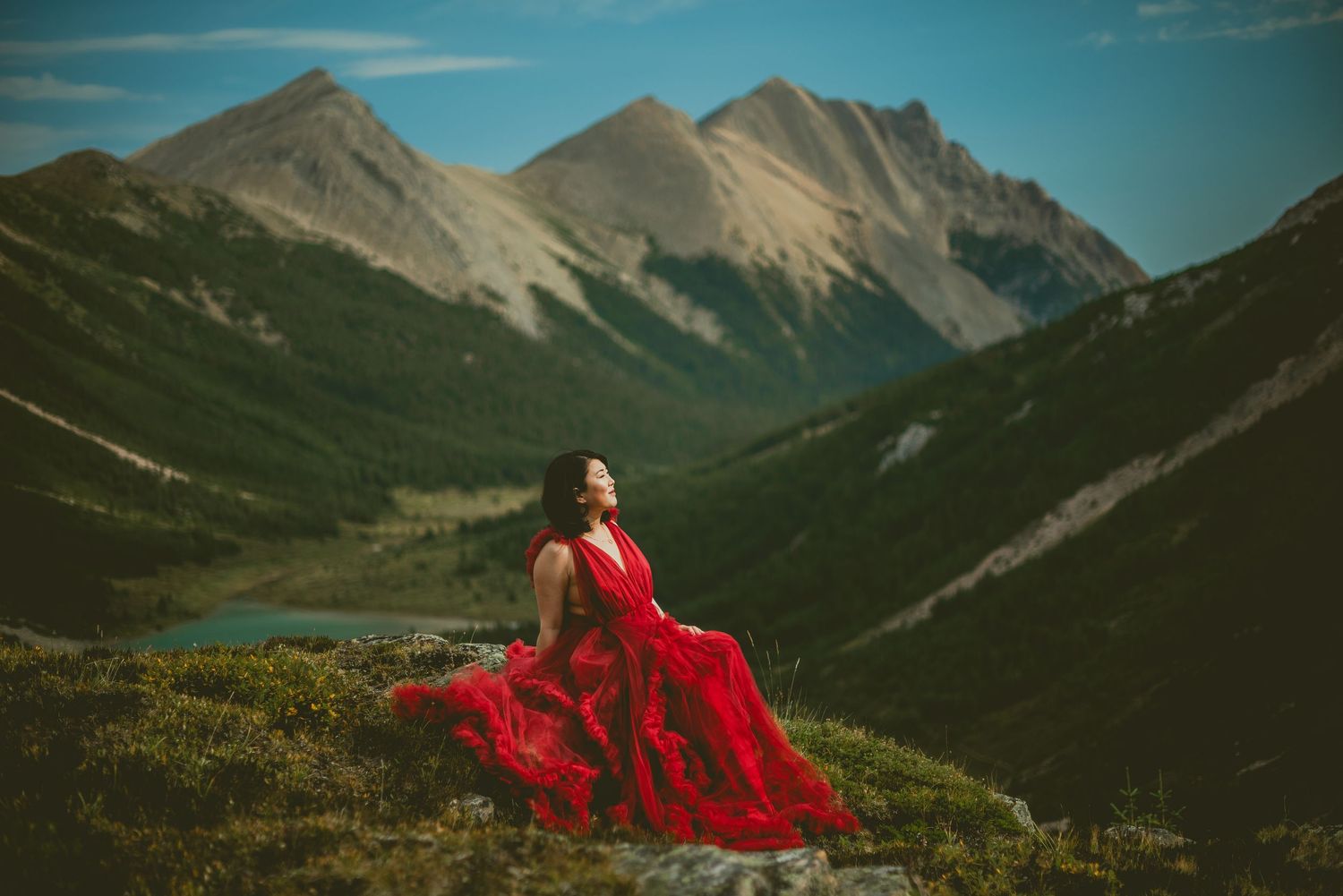A flowing red dress against rugged mountain peaks and alpine meadows in a scenic landscape. Alberta Helicopter Elopement Photographer