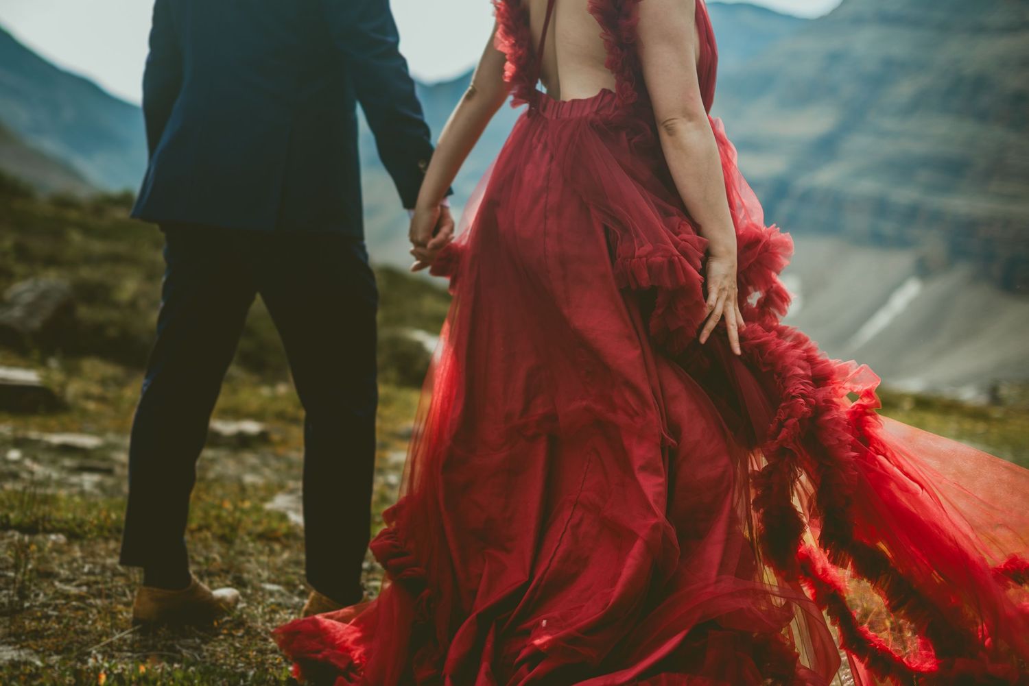 A red flowy dress creates dramatic contrast against rugged mountain scenery Alberta Helicopter Elopement Photographer