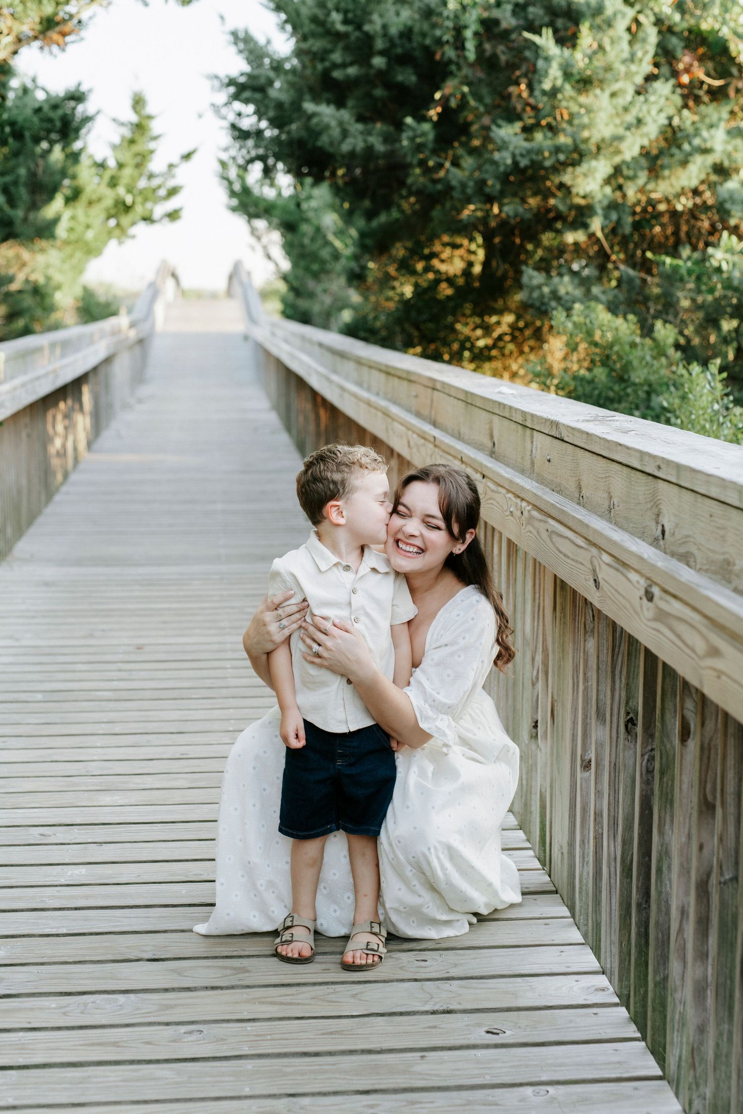 A tender moment shared between parent and child on a wooden bridge walkway surrounded by evergreen trees.