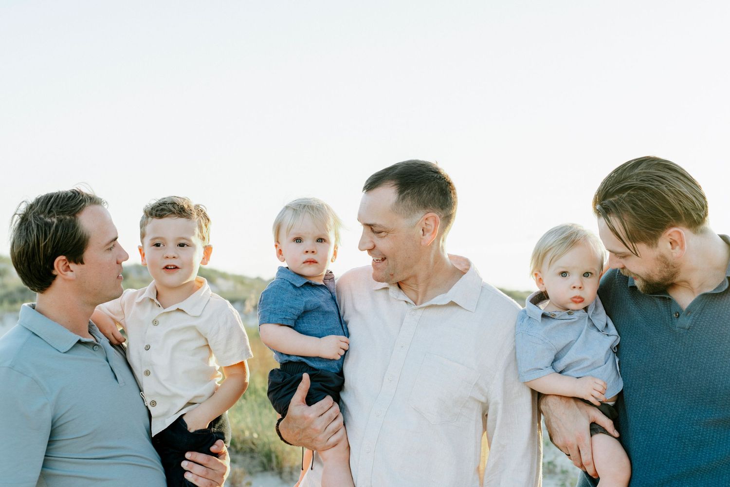A family group in blue and white clothing poses together in a grassy field during golden hour.
