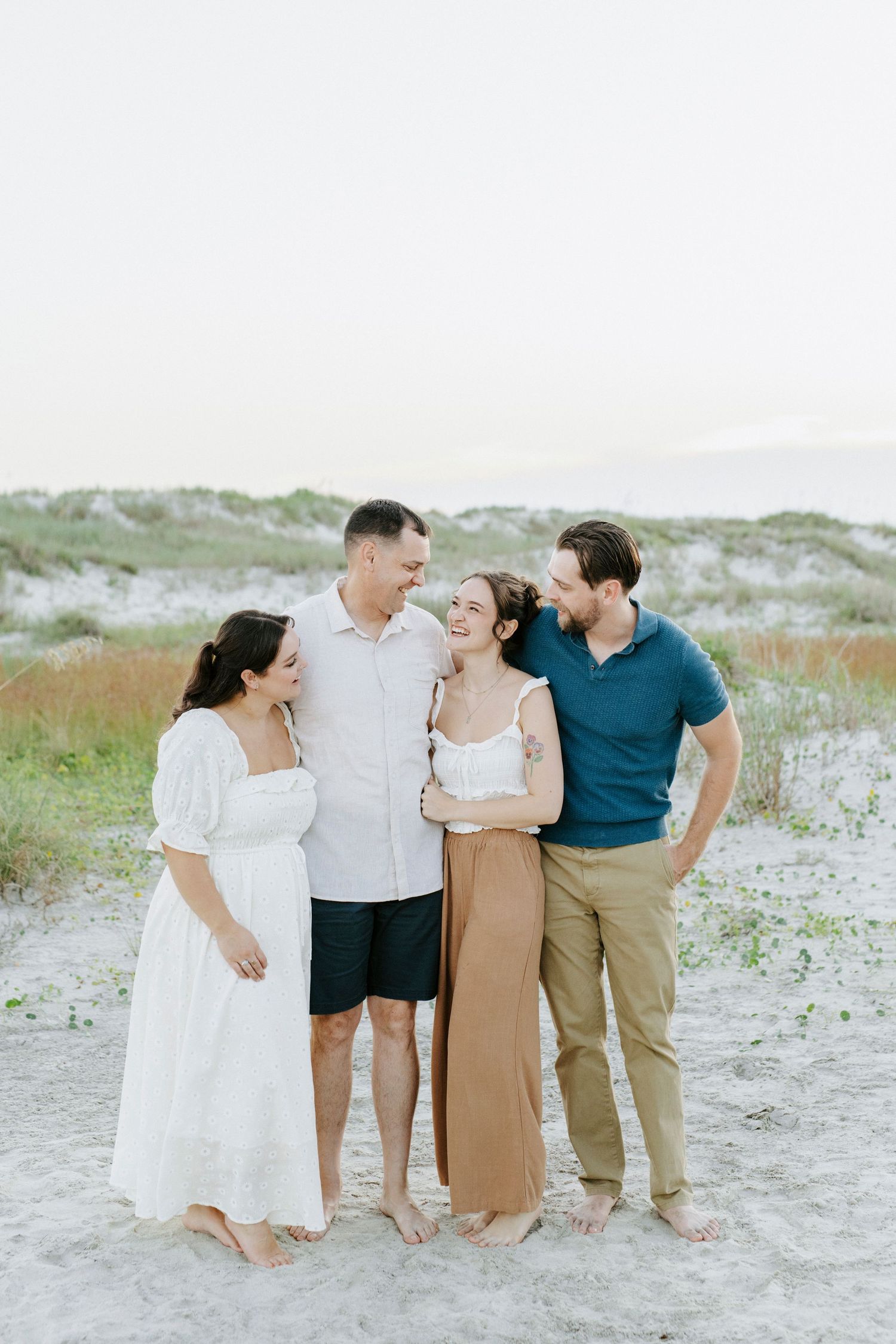 Group of friends sharing laughter together on a sandy beach at dusk.