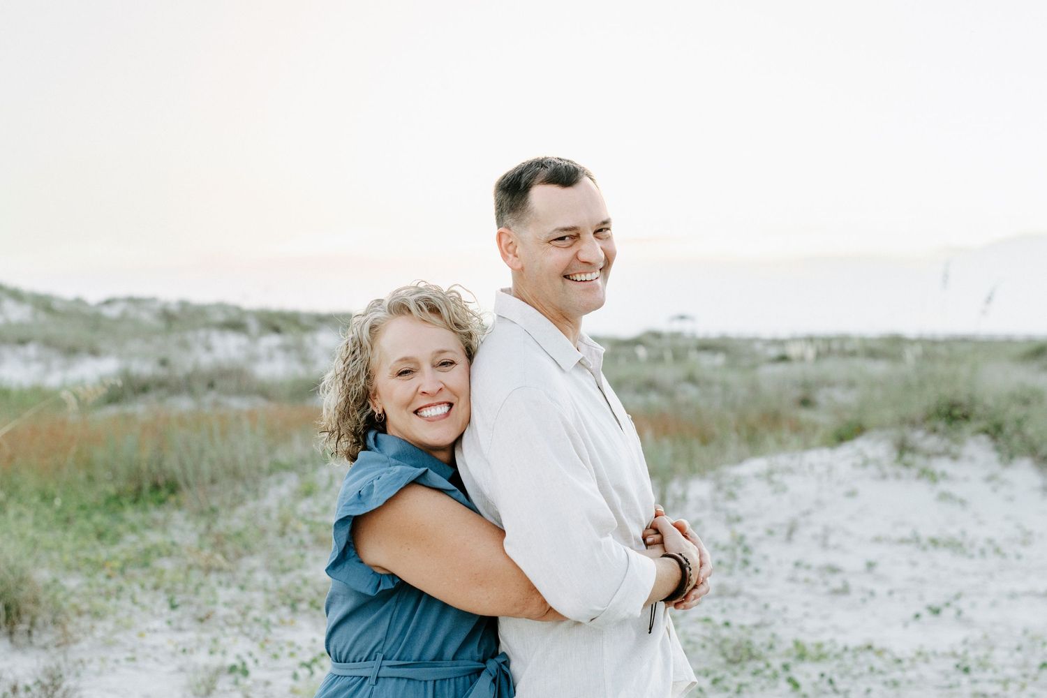 Couple walking and embracing on sandy beach path during sunset photo session.