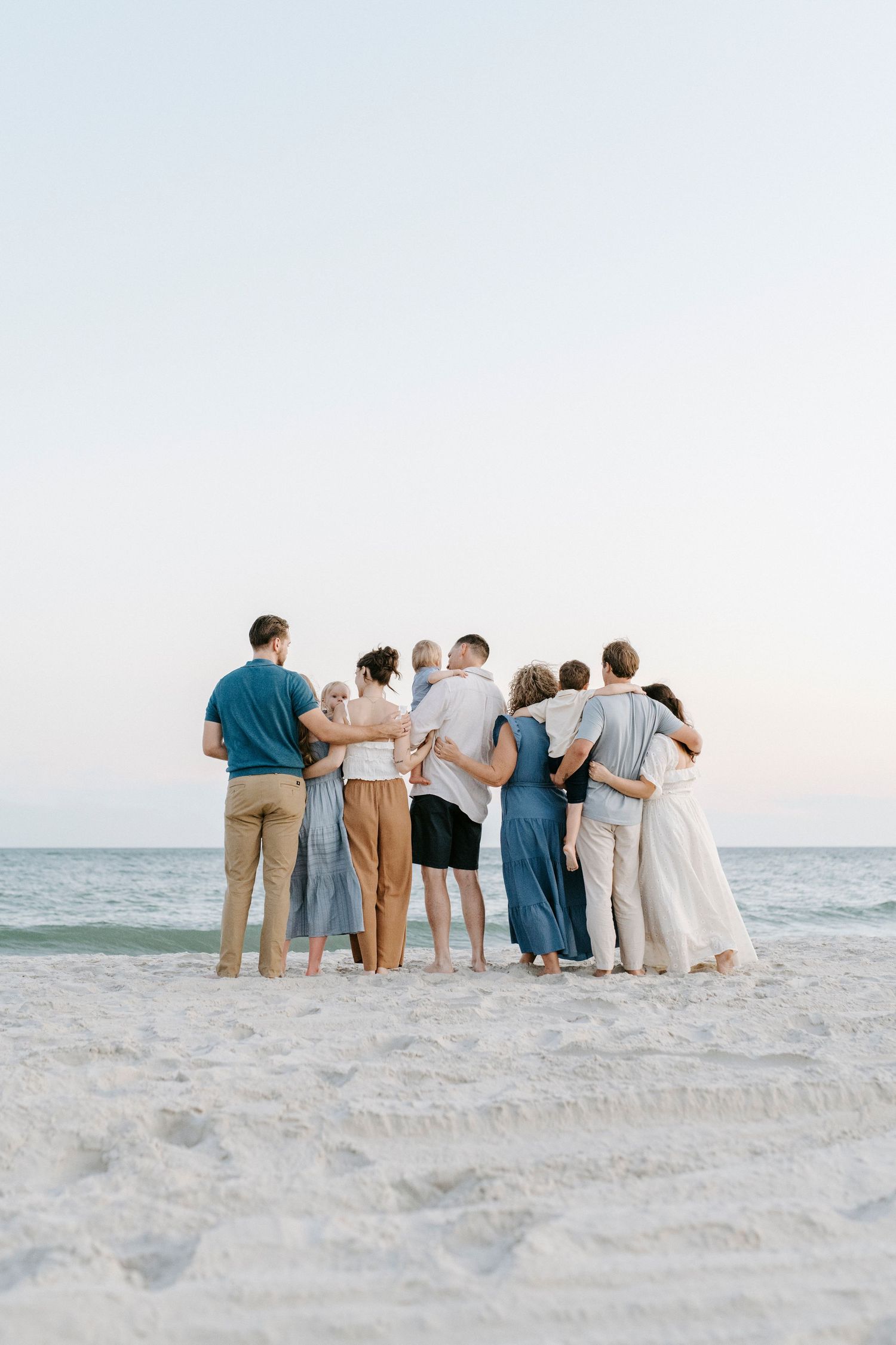 A group of people stand together on a white sandy beach with ocean views while huddled in a close formation.