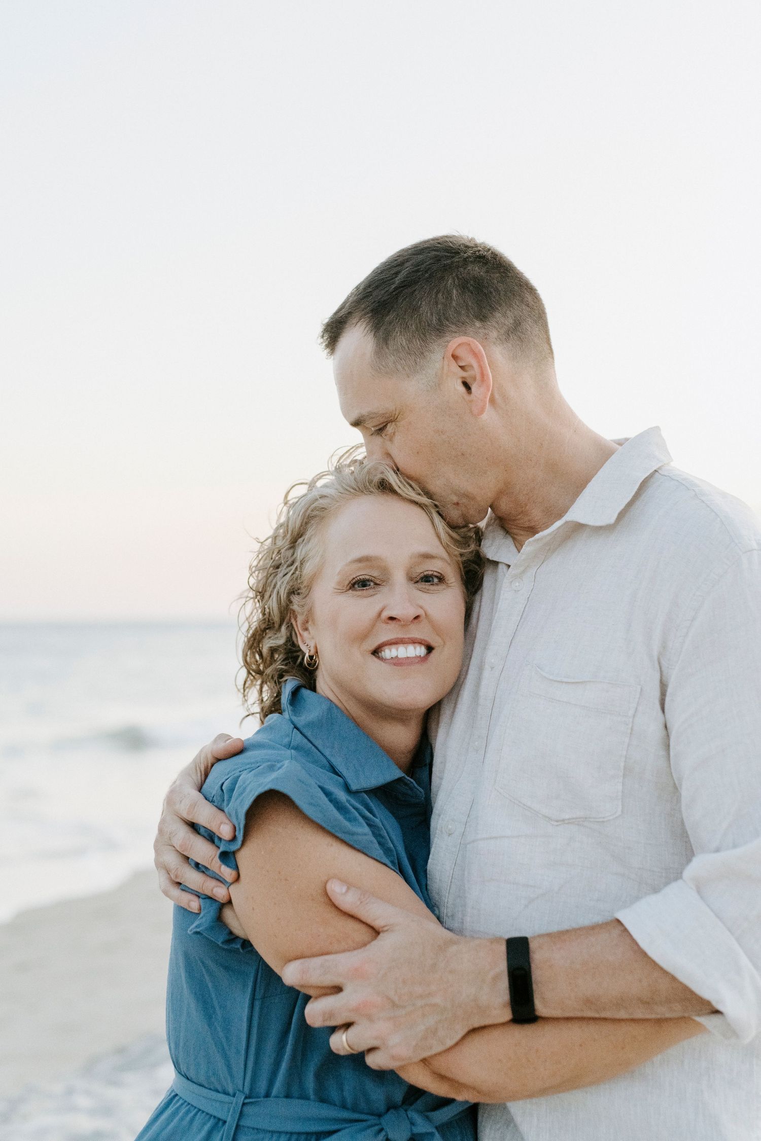 An intimate moment between a couple embracing on the beach at sunset.