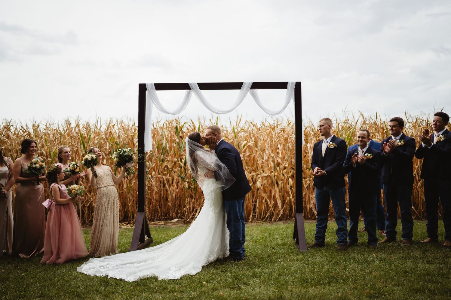 Wedding party poses in front of golden corn field during autumn sunset ceremony.