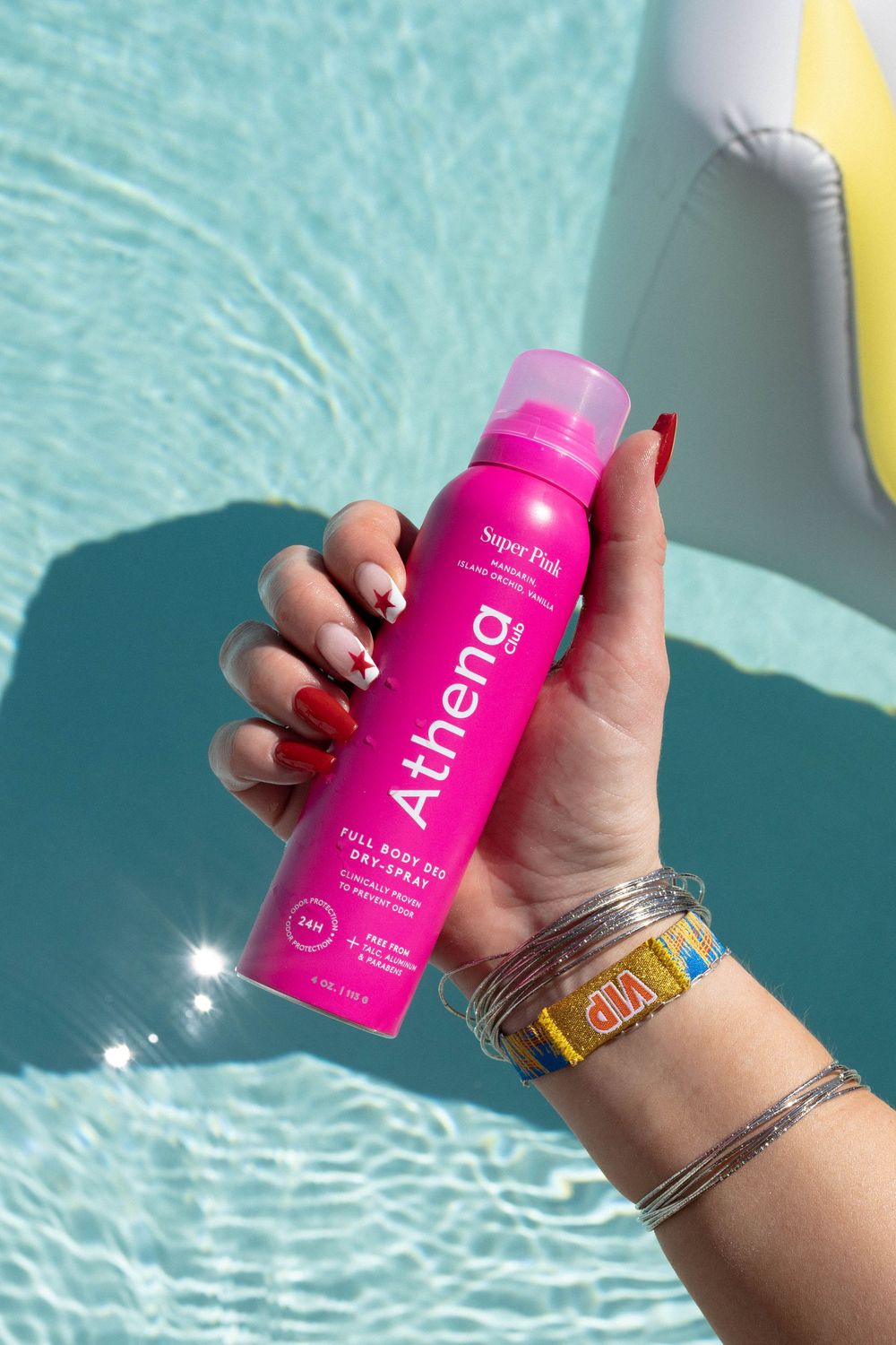 Hand holding a bright pink Athia skincare product bottle against a blue swimming pool background.