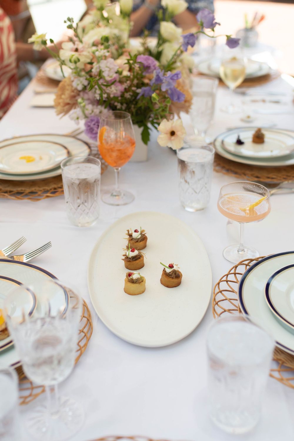 Elegant table setting with delicate floral arrangements and fine china on white tablecloth.