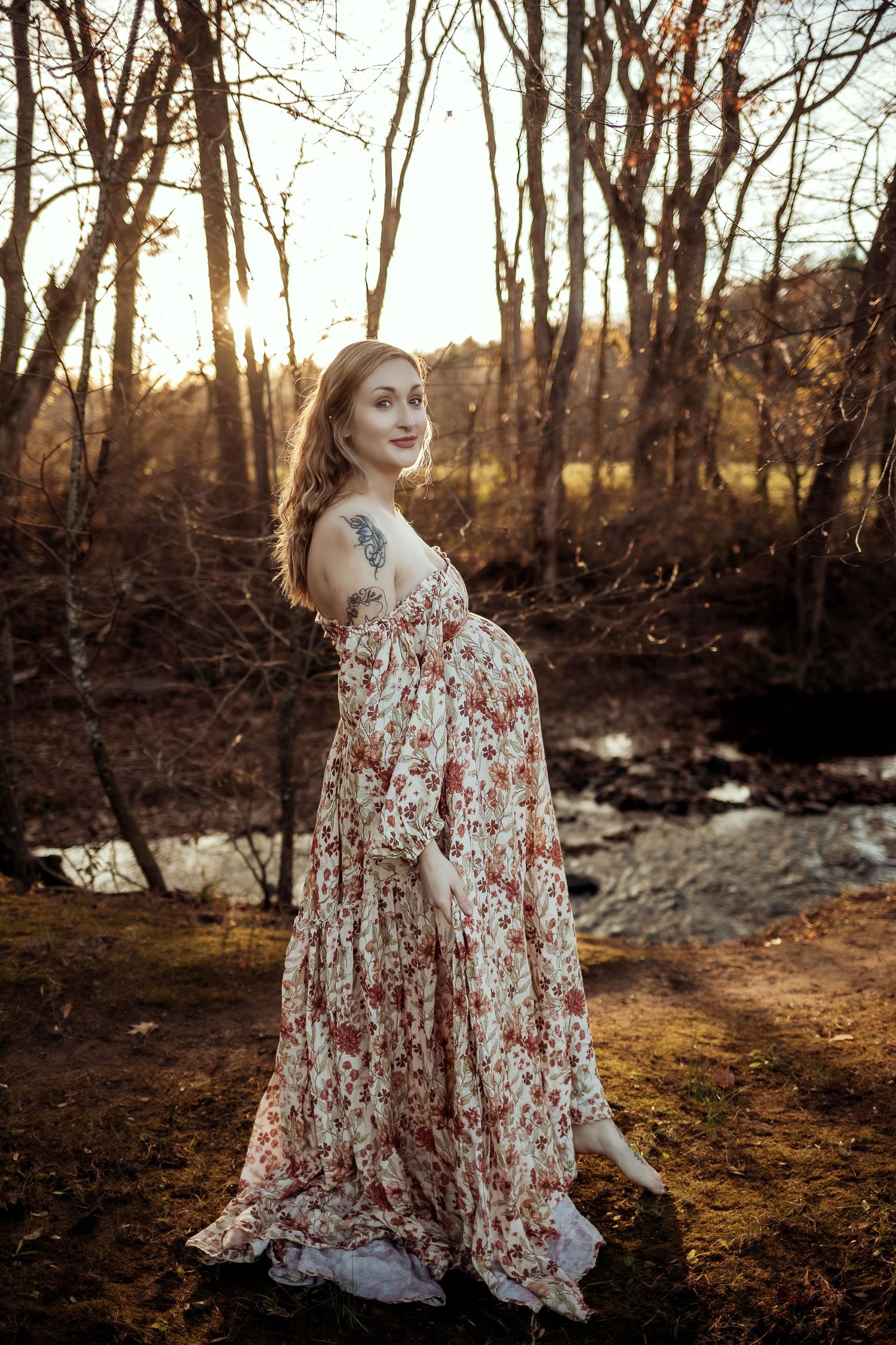 A floral dress flows gracefully in the autumn woods during golden hour as sunlight filters through bare trees.