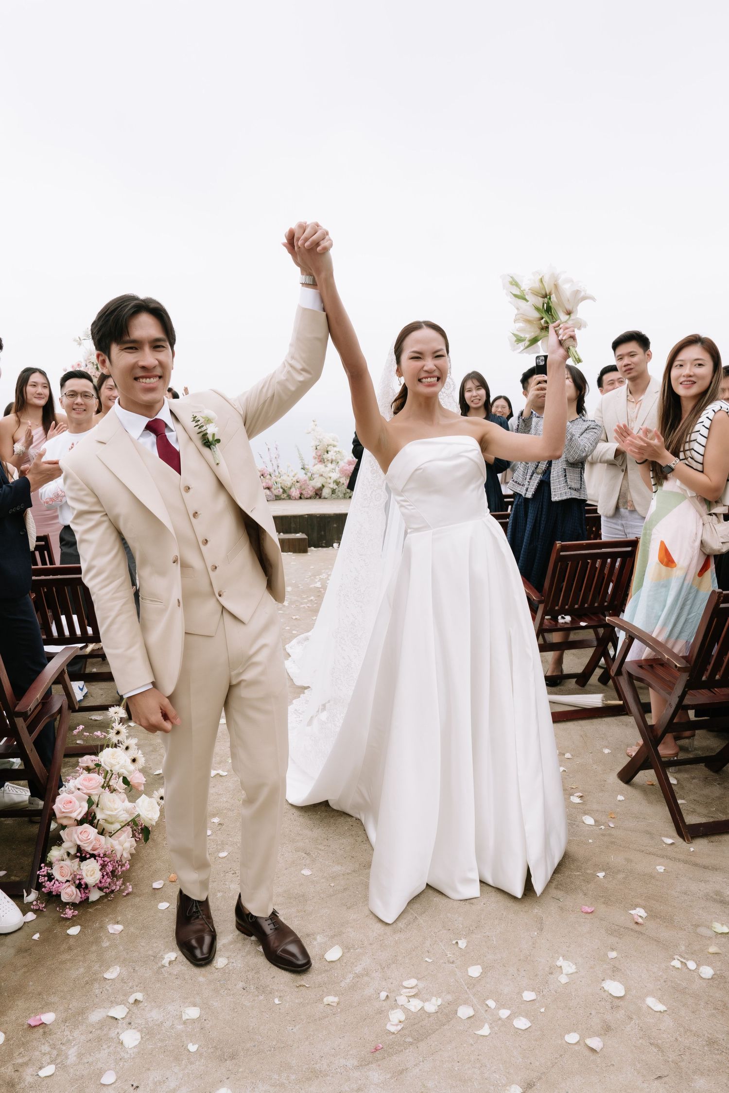 Jubilant newlyweds raising hands in celebration as guests cheer at an elegant outdoor wedding ceremony.
