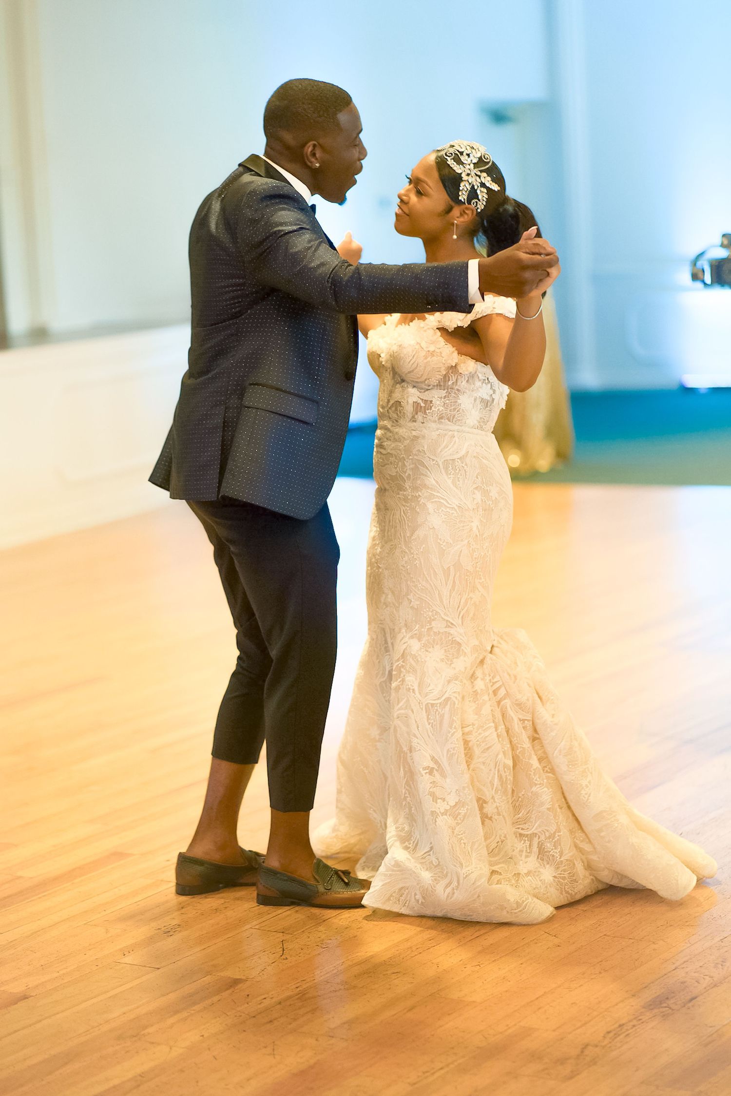 A couple dances together in an elegant ballroom with wooden floors.