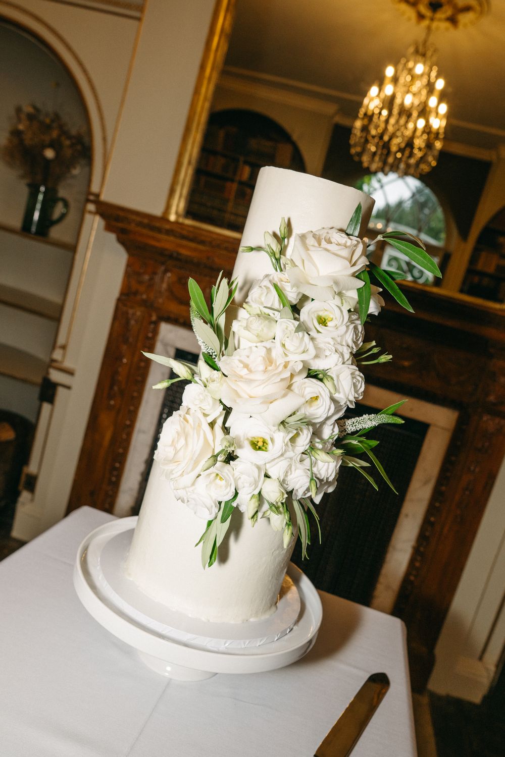 White wedding cake with delicate floral decorations and greenery shown from multiple angles on a light surface.