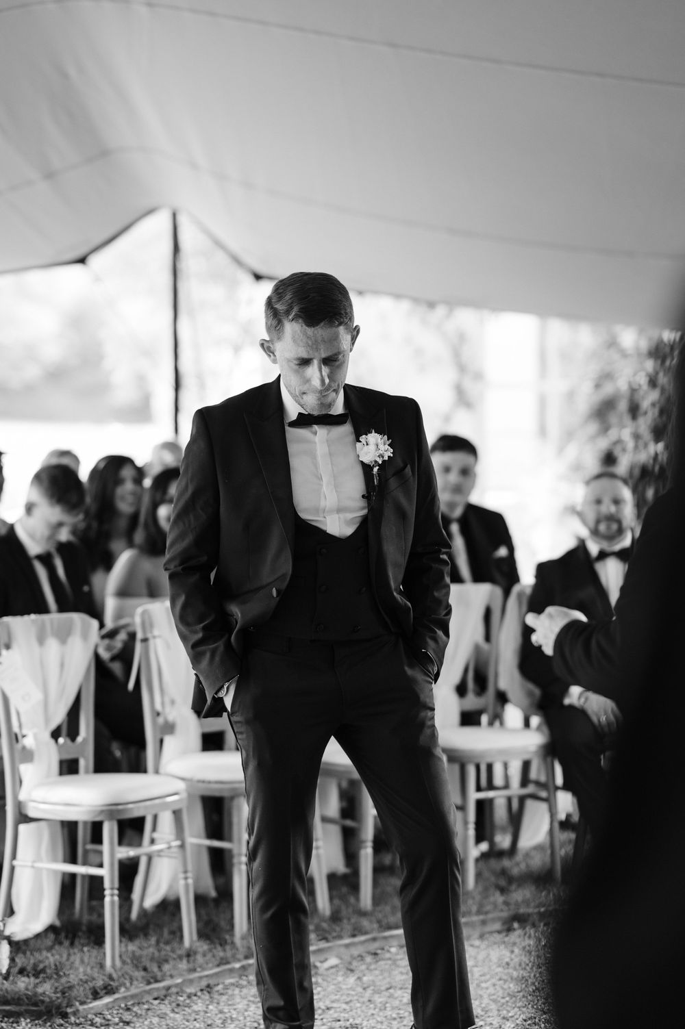 Black and white photograph of groomsmen in tuxedos gathered at an outdoor wedding reception ceremony under a tent.