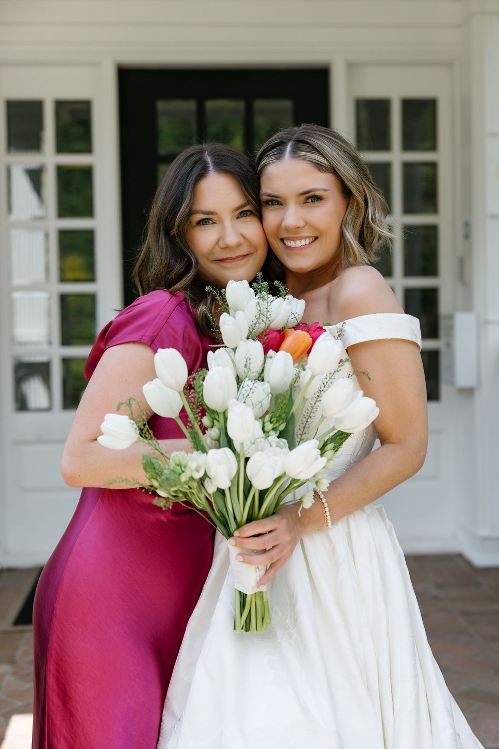 Bridesmaids in burgundy dresses pose with bride in white gown holding white tulip bouquets at wedding.