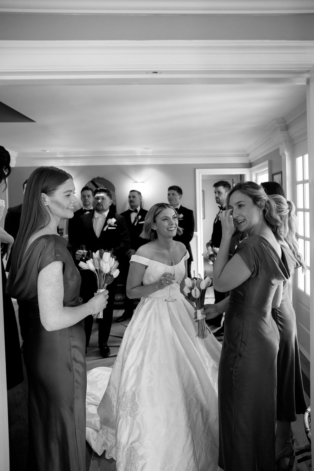 Wedding party gathers indoors for celebratory moments in an elegant white-walled venue.