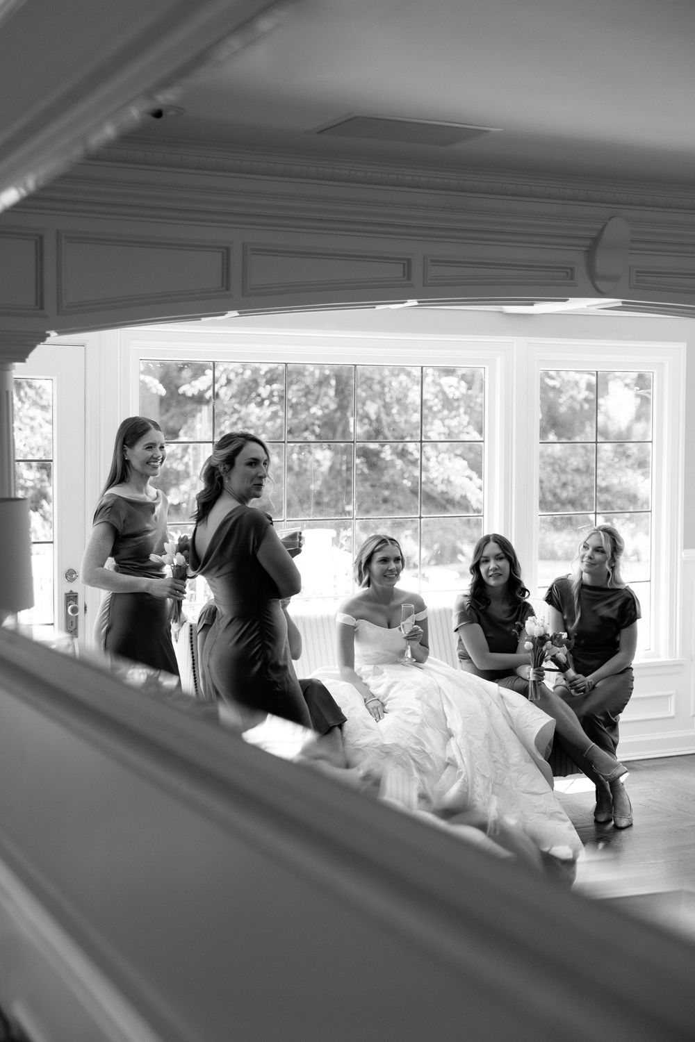 A black and white photo series showing a joyful gathering of people laughing and embracing in a sunlit room.