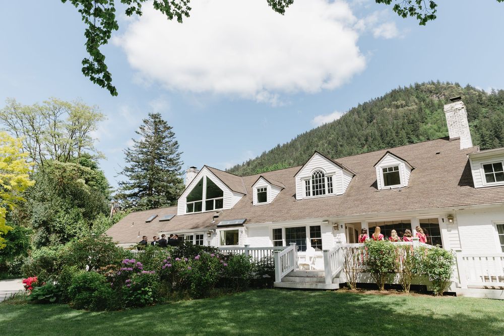 Panoramic view of white colonial style wedding venue with dormers under blue summer sky.