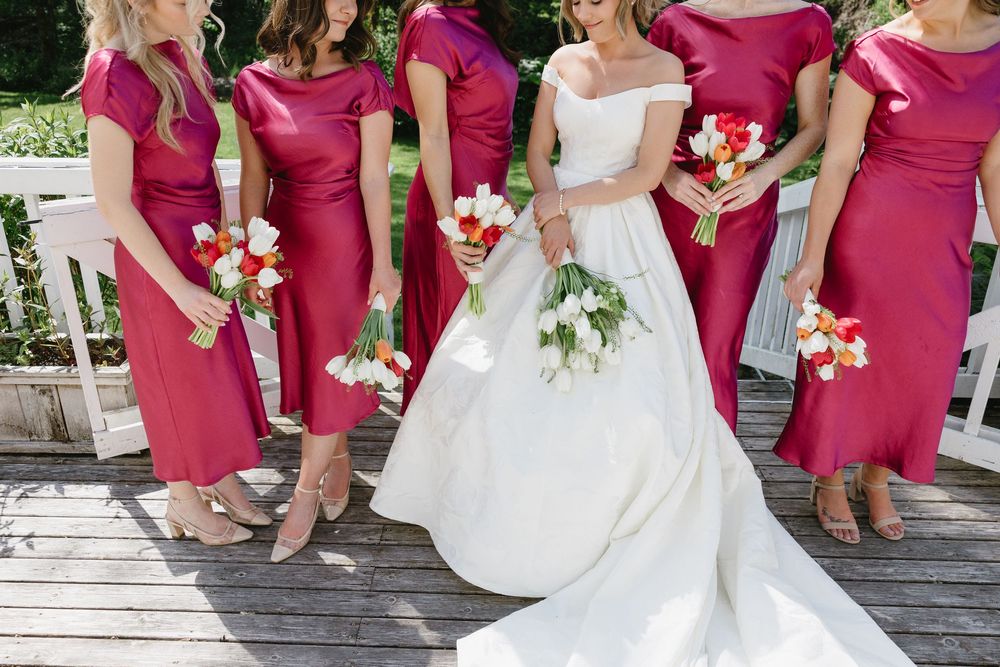 Wedding party in burgundy dresses and white gown lined up on outdoor wooden deck.
