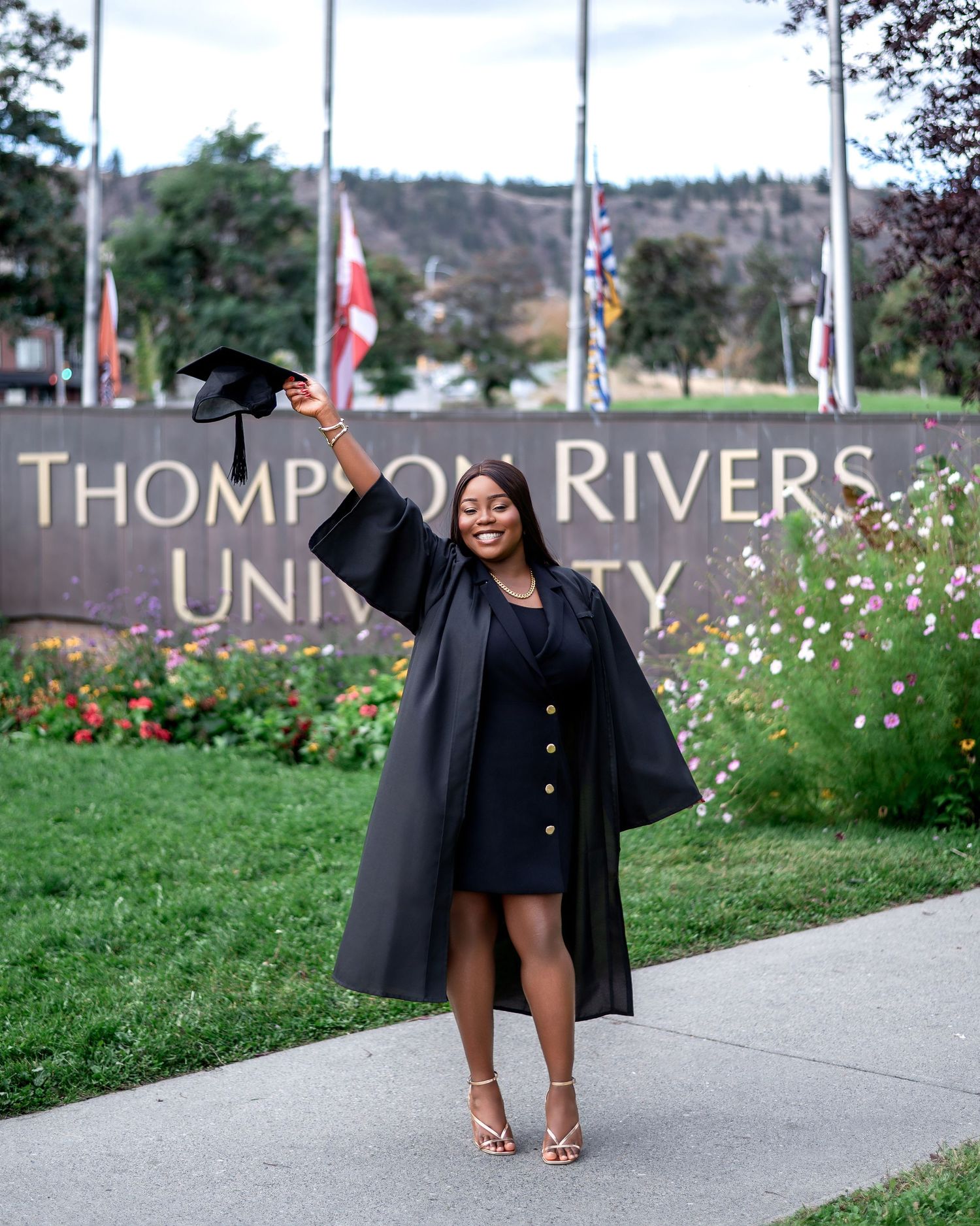 Graduate walks confidently past Thompson Rivers University sign in black academic attire.