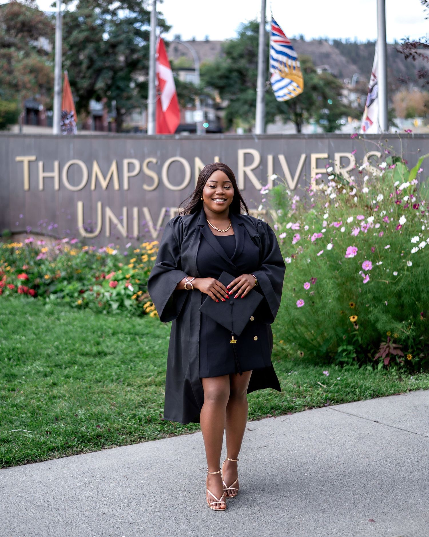 Graduation photoshoot at Thompson Rivers University with flags and flowers in background.