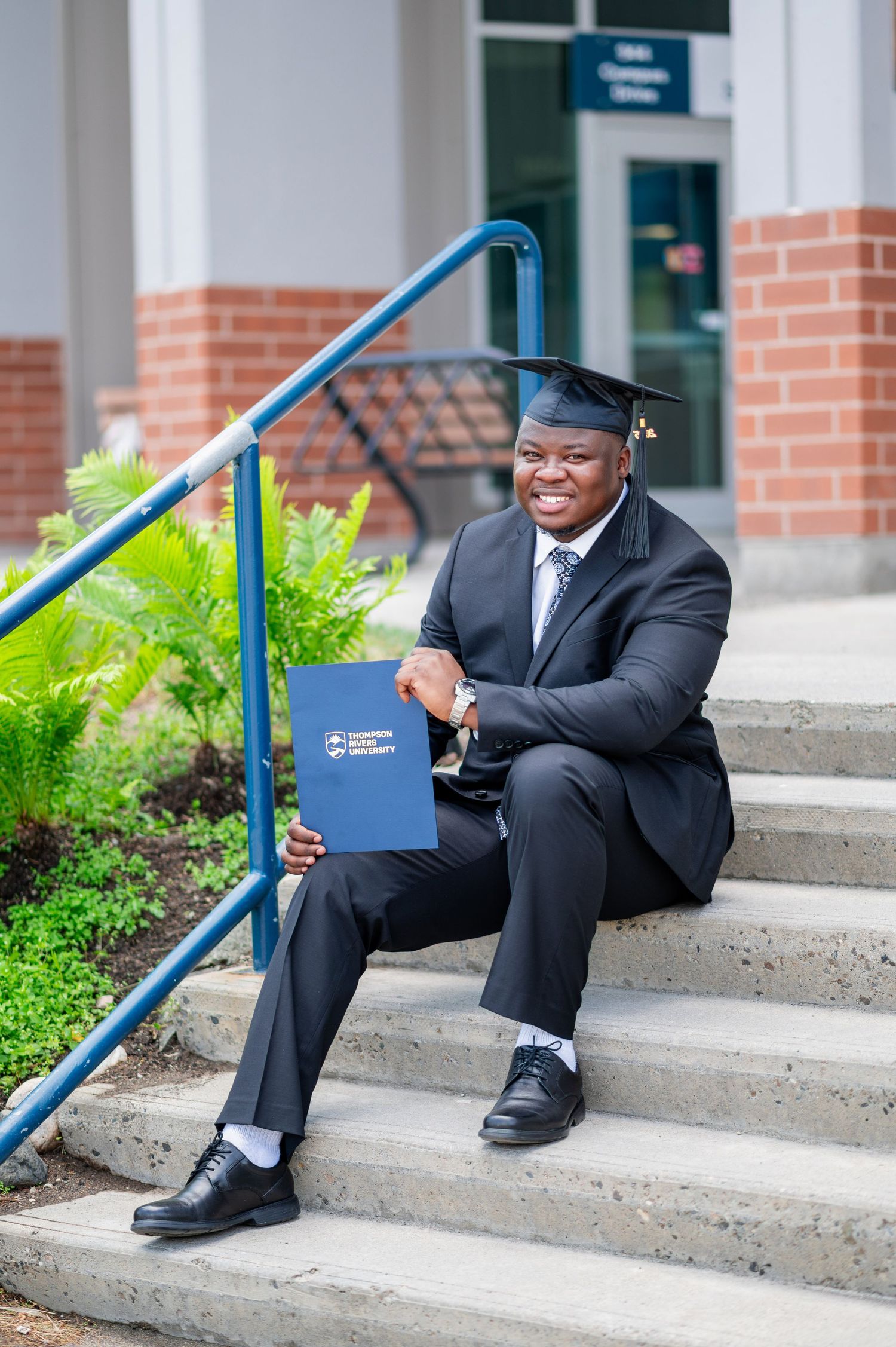 Graduate seated on steps holding diploma while wearing traditional academic regalia.
