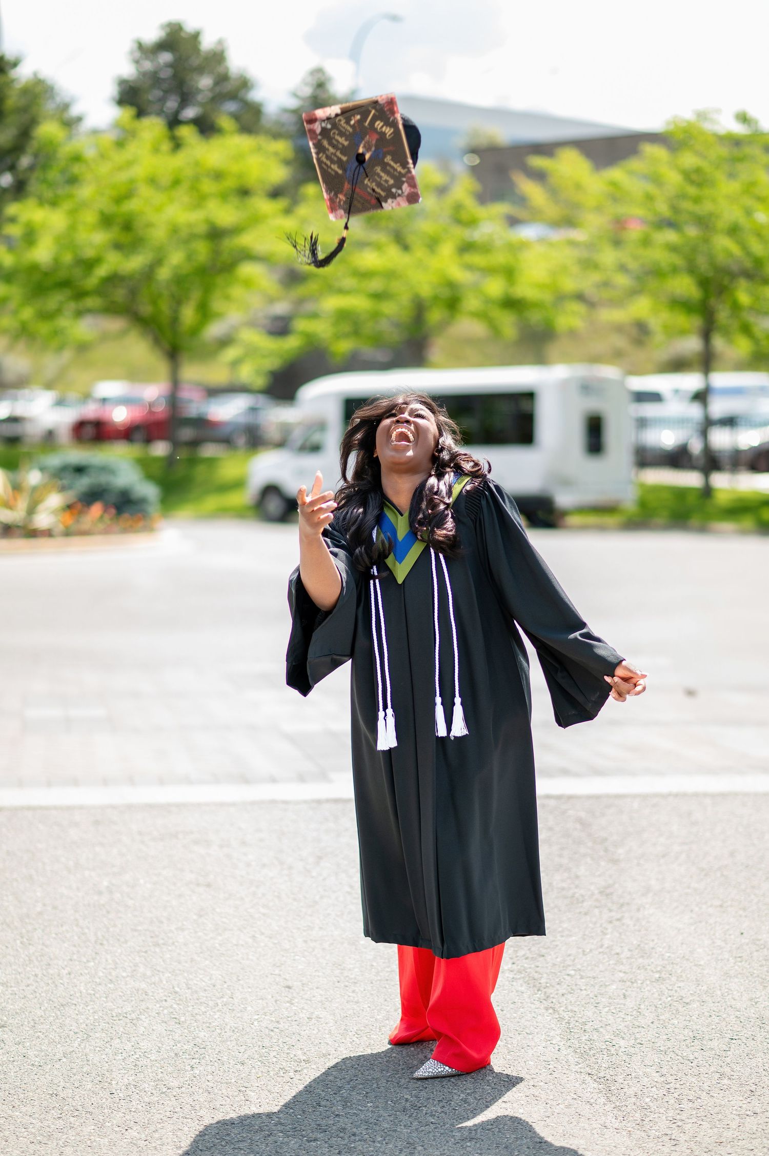 Graduate in cap and gown jumps joyfully in parking lot during celebration photoshoot.