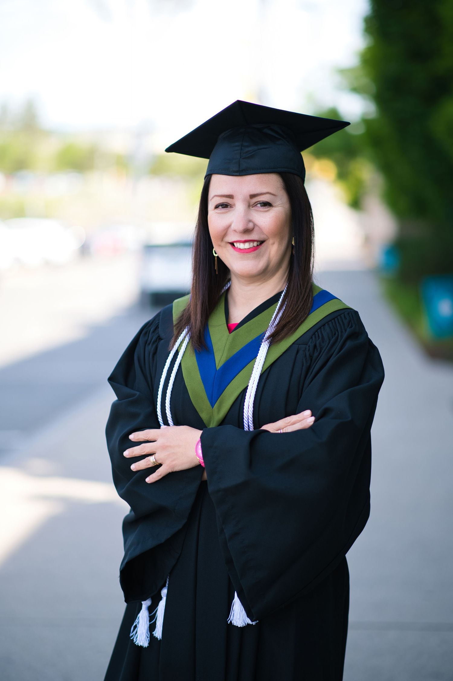 Graduate in traditional black academic regalia poses outdoors.