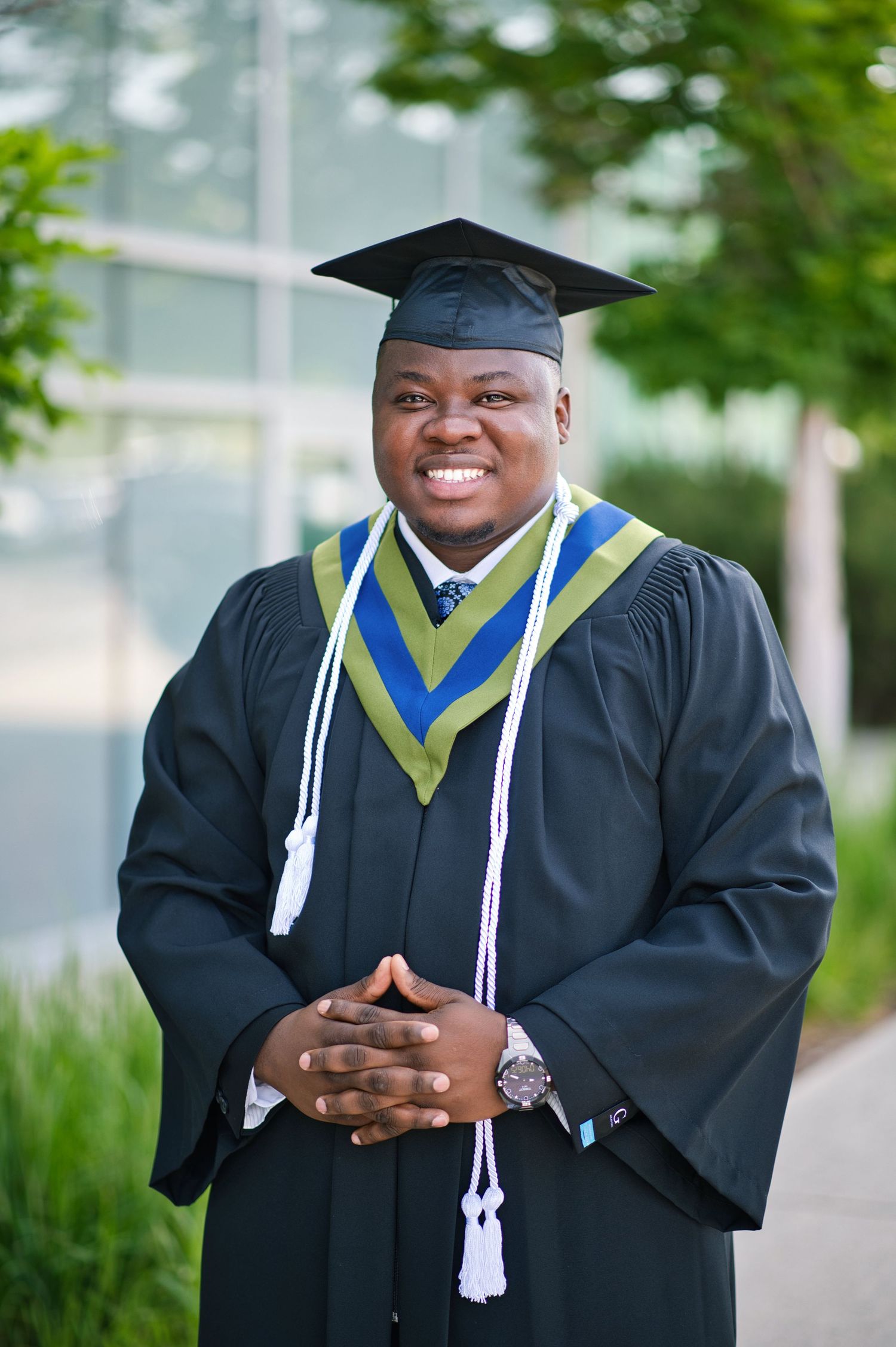 Graduate in academic regalia smiles warmly during outdoor graduation photoshoot.