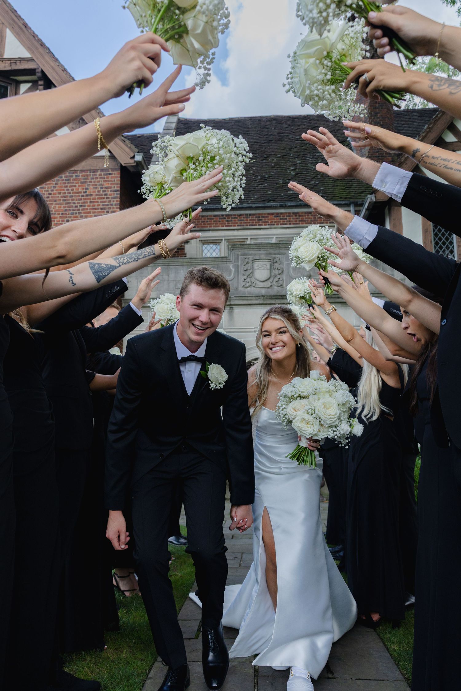 Wedding couple walks through a tunnel of raised arms formed by guests in black attire during their celebration exit.