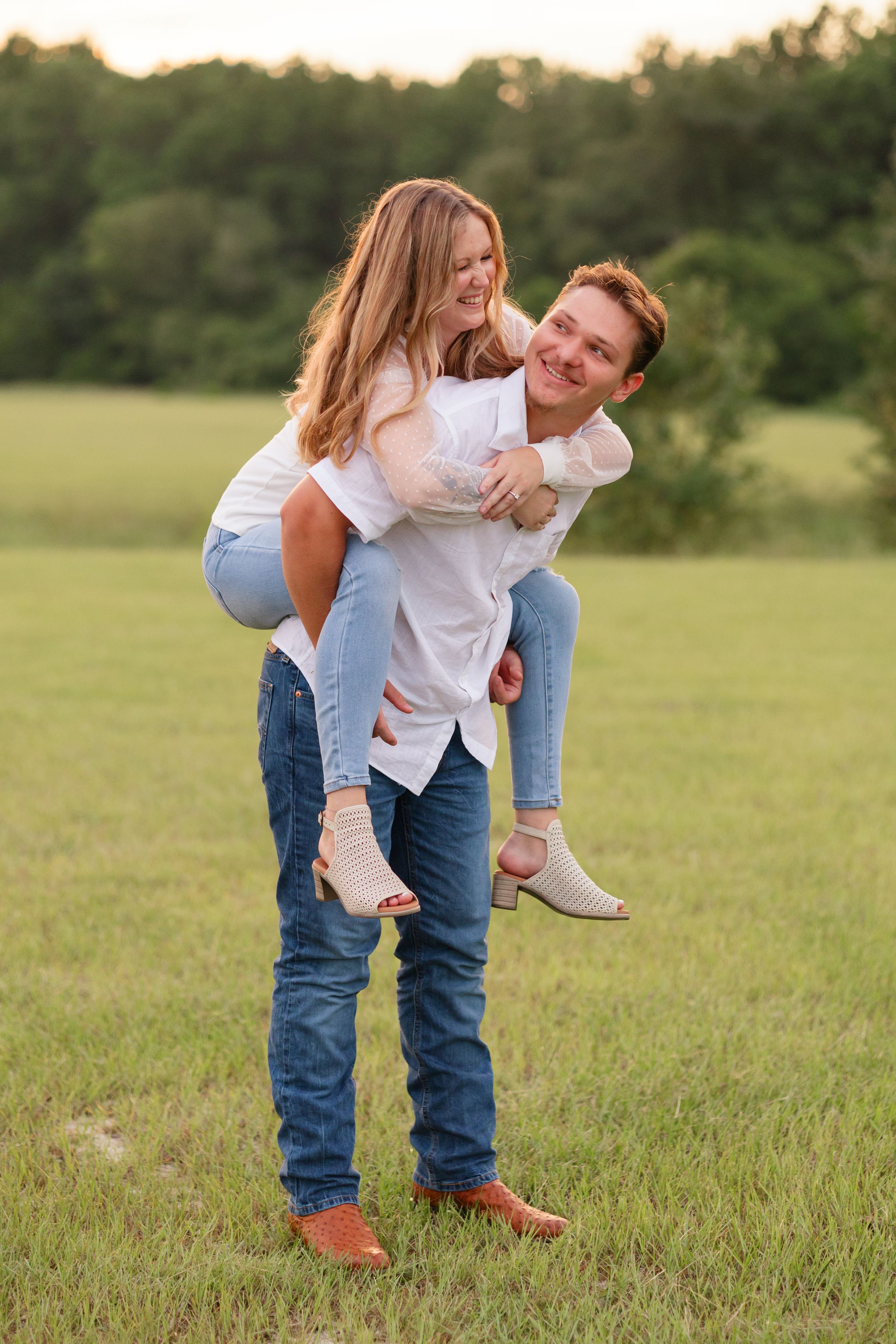 Couple enjoying lighthearted piggyback rides and laughter in a green meadow at sunset.
