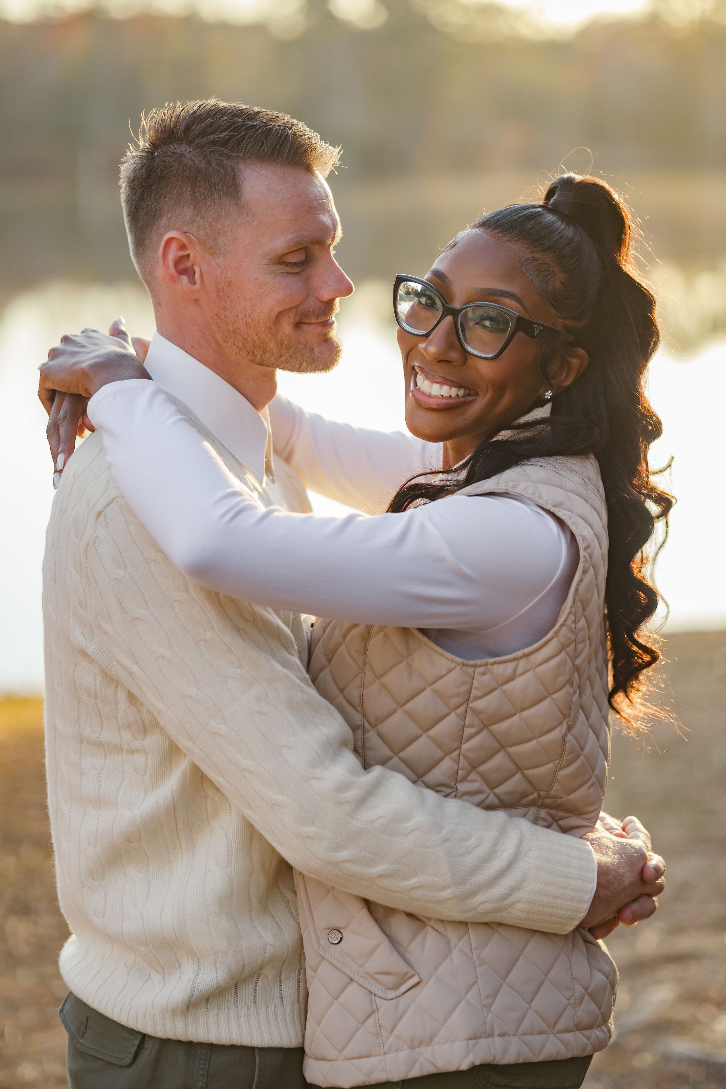 A couple embraces outdoors wearing matching quilted vests during golden hour sunset.