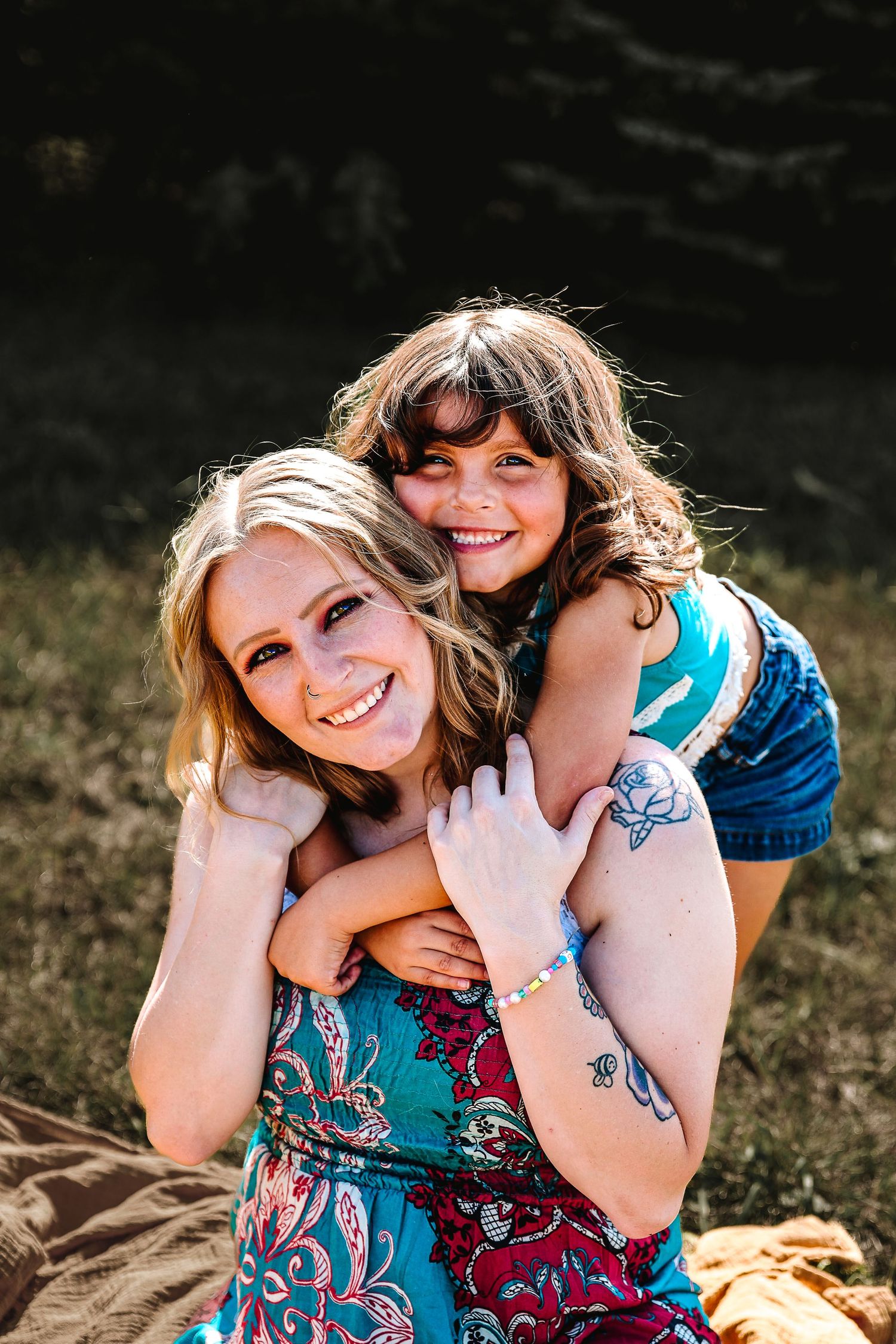 Two people embrace outdoors while sitting on a blanket during golden hour photography session.
