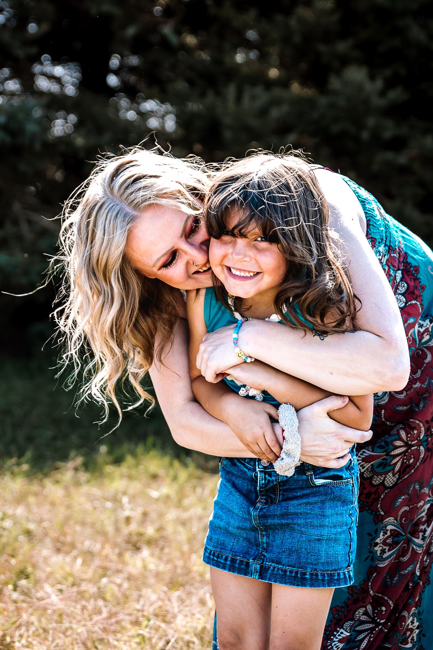 Two friends share joyful moments together in a sunny field wearing casual denim and floral outfits.
