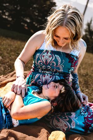 Two people in teal and black patterned clothing embrace while lying on the ground during an outdoor photoshoot.