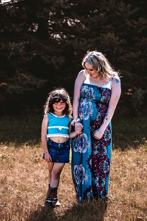 Two people wearing coordinating blue patterned outfits stand together in a sunny outdoor field at sunset.