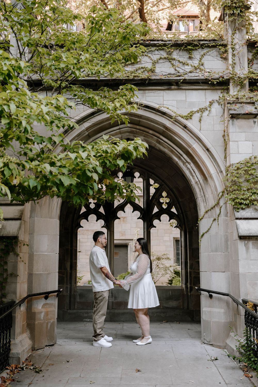 Couple shares a romantic moment in front of a Gothic stone archway surrounded by green foliage.