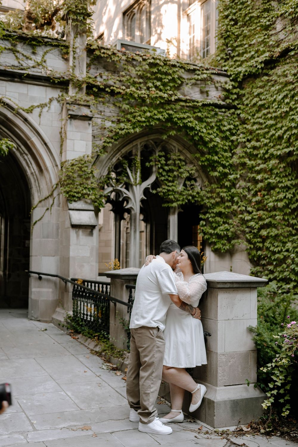 A romantic couple shares intimate moments along a stone archway corridor with ivy-covered walls.