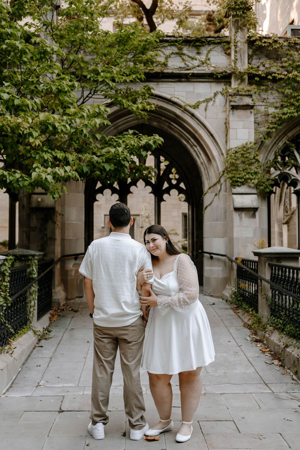 Two people stand together in a historic stone courtyard with arched architectural details.