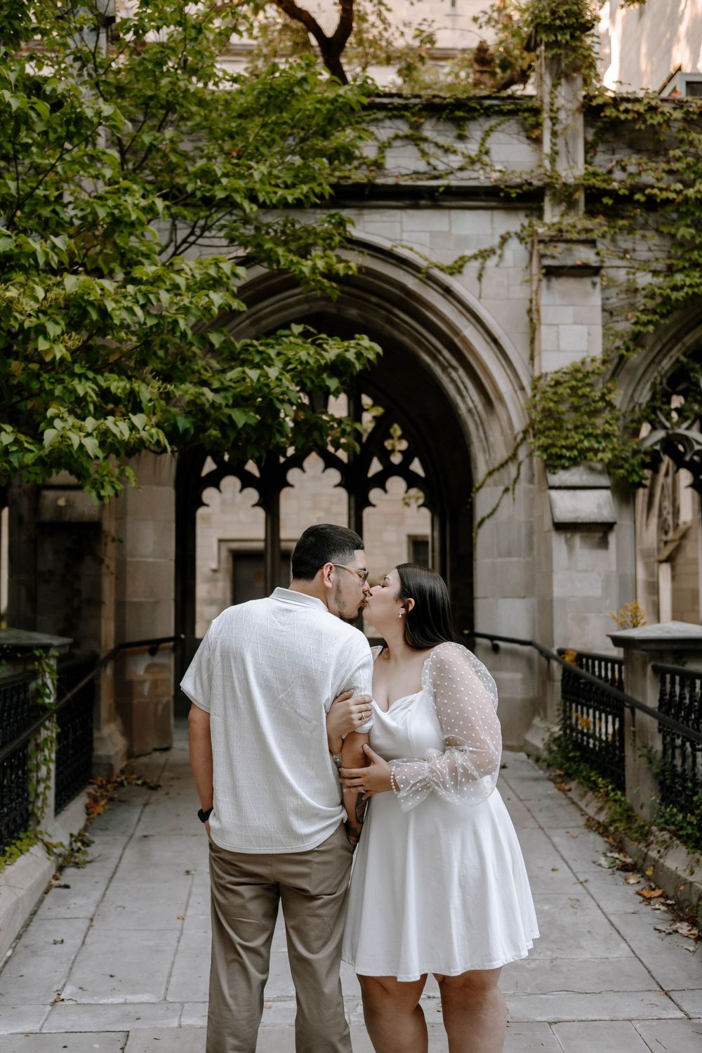 A couple poses together in a gothic stone hallway with climbing vines and arched architecture.