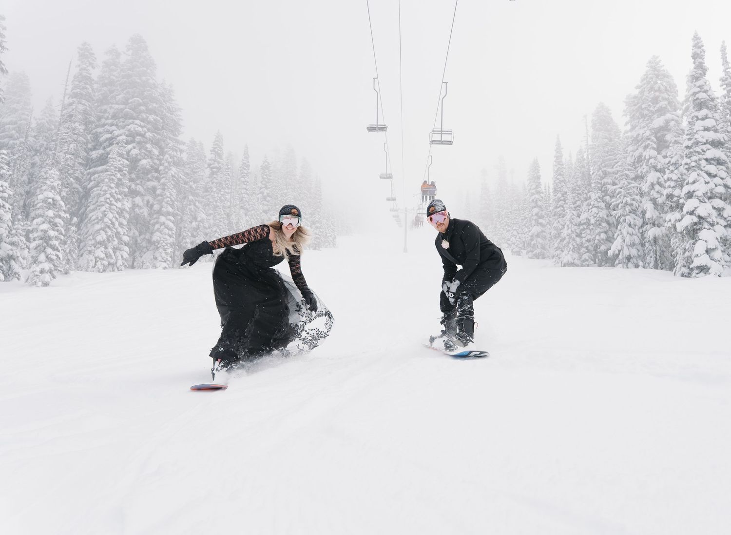 Snowboarders carving through fresh powder on a snowy mountain slope during winter sports action.