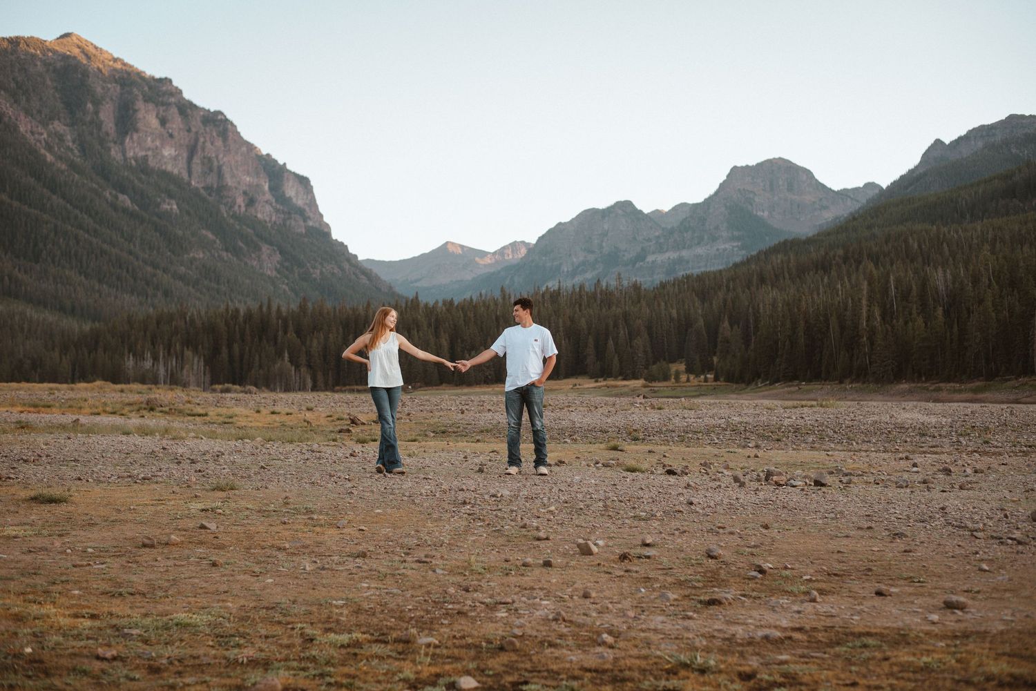 A couple dances in a scenic mountain valley with evergreen forests and rocky peaks.