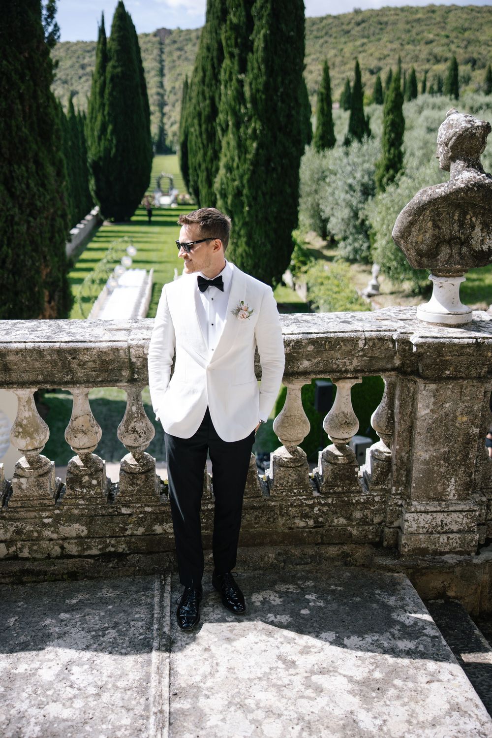 Elegant wedding attire on display at a grand Italian villa with cypress trees and stone balustrade.