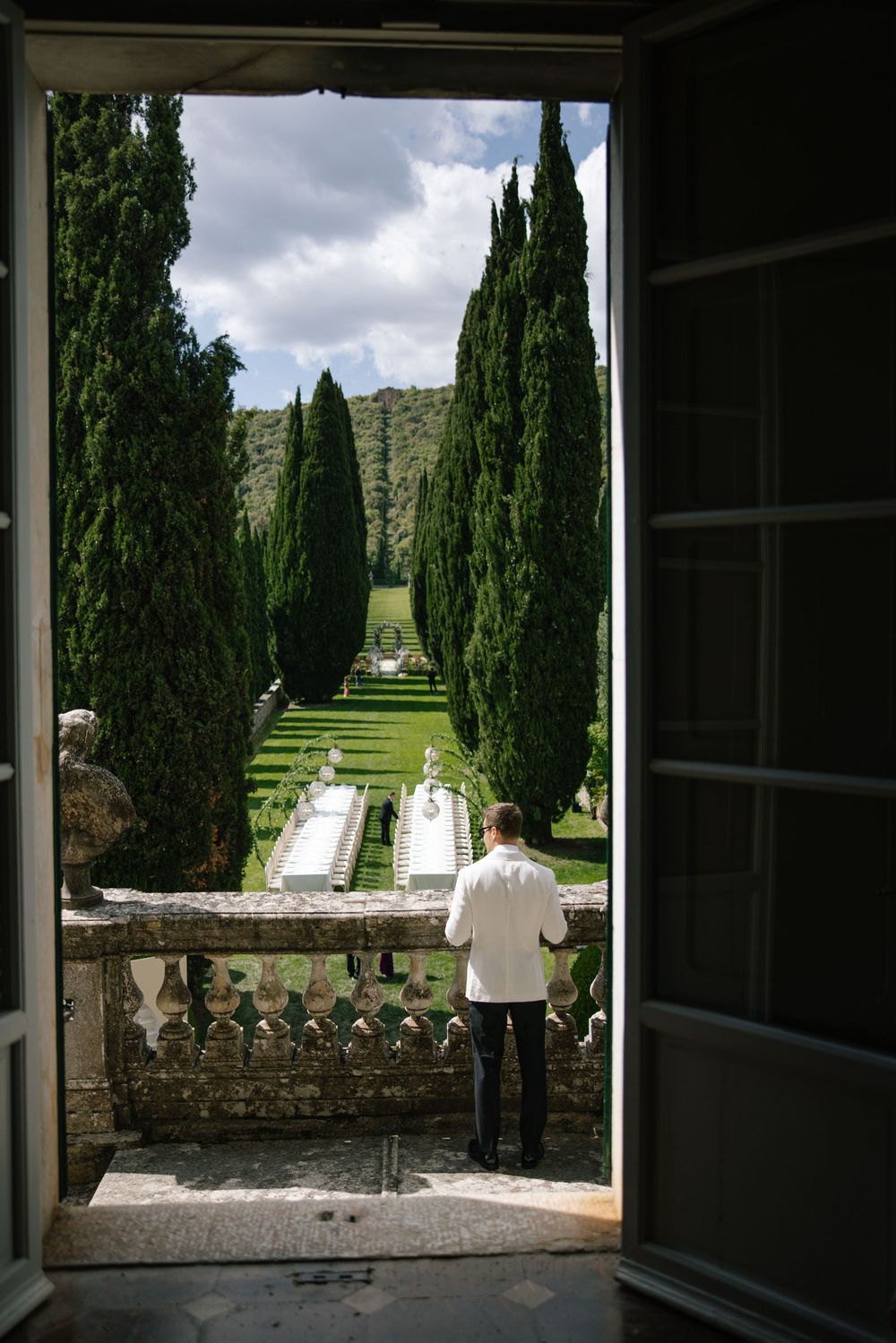 View through doorway of Italian garden with cypress-lined path and stone balustrade.