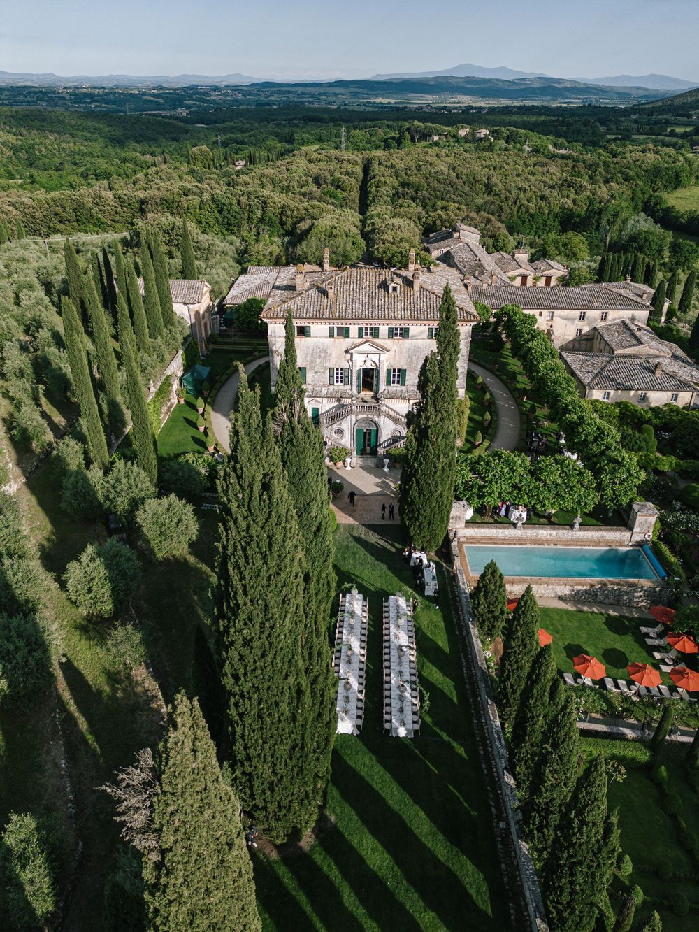 Aerial view of a luxurious Tuscan villa with cypress trees, swimming pool and wedding ceremony setup.