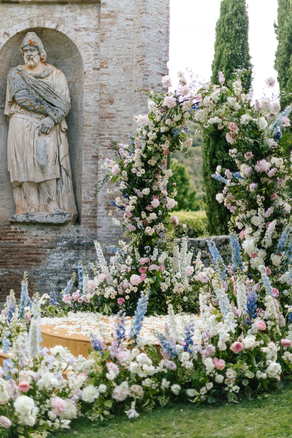 Luxurious floral arrangements with pink roses and blue delphiniums decorating stone archways.