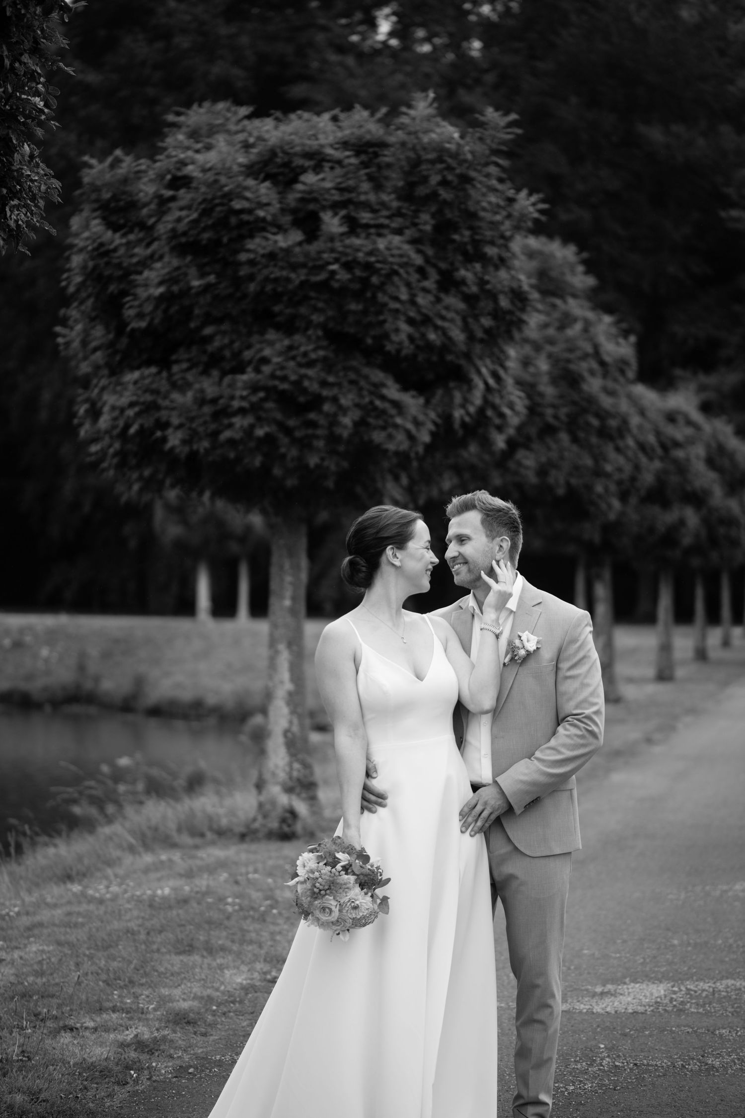 A couple in wedding attire share intimate moments while walking along an outdoor path in a romantic photoshoot.