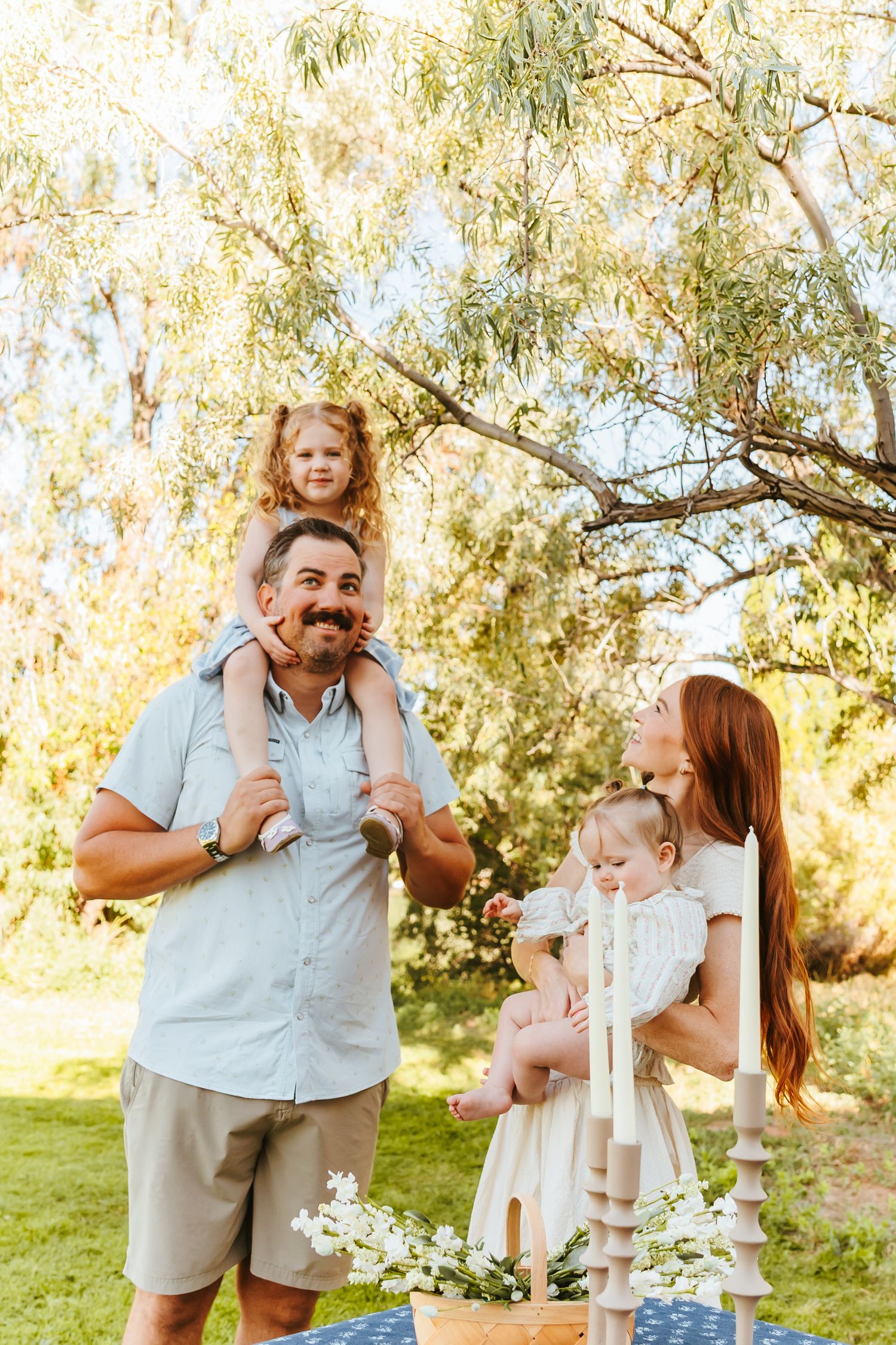 A family shares joyful moments together in a sunny outdoor setting with willow trees in the background.