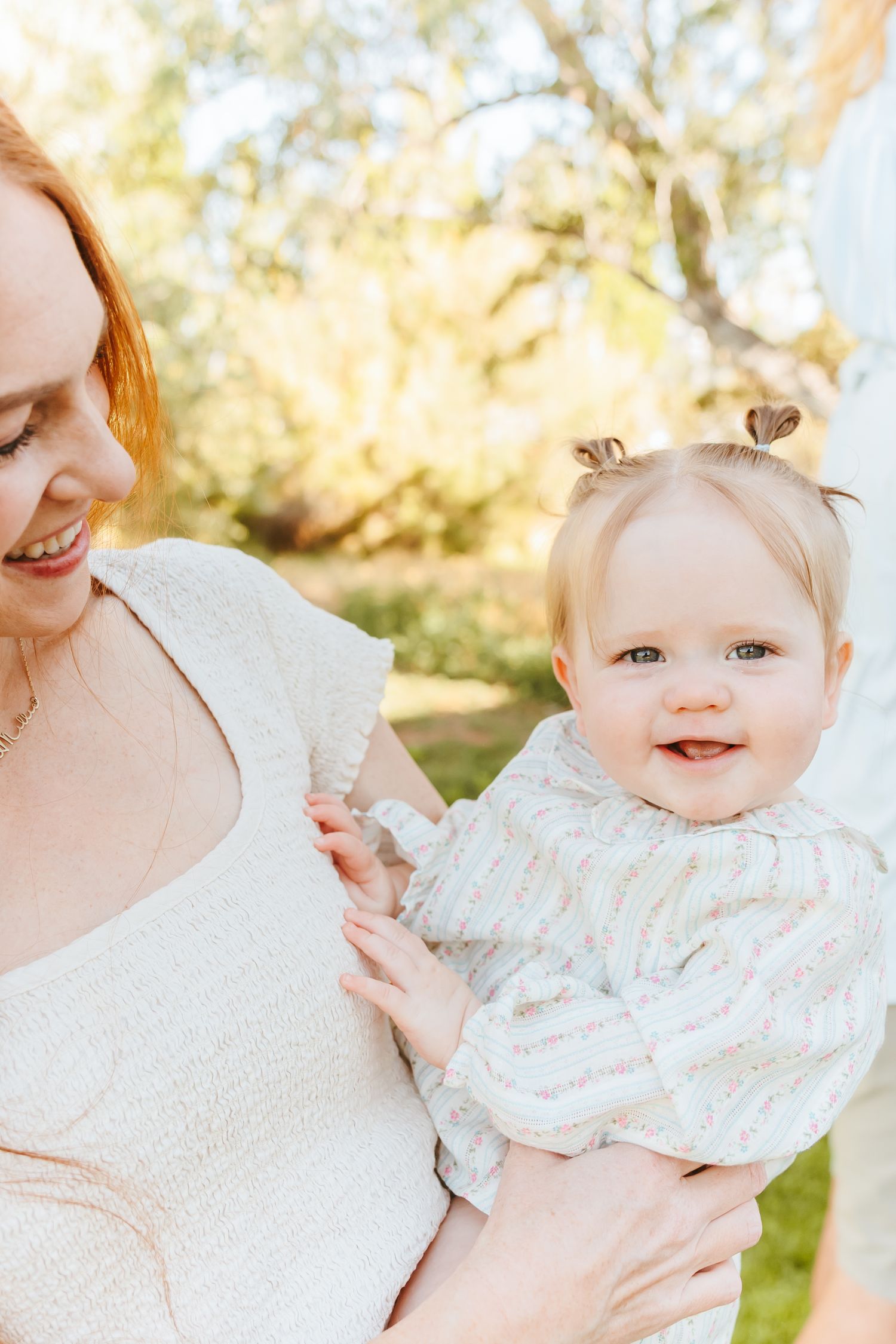 A tender moment between parent and baby in white clothing captured outdoors in soft natural lighting.