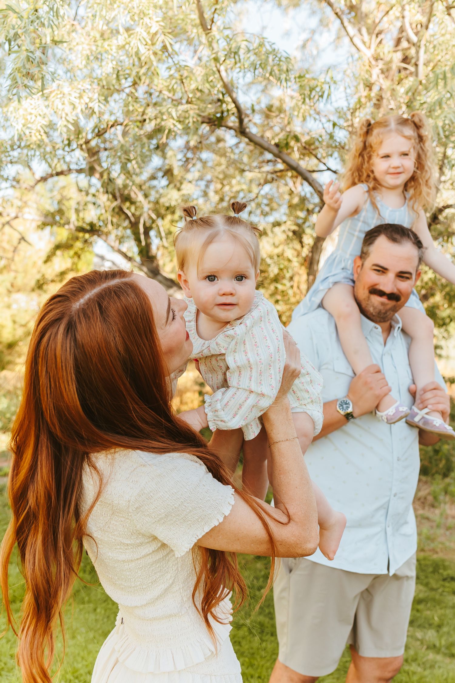A joyful family moment captured outdoors with playful interactions in golden sunlight among olive trees.