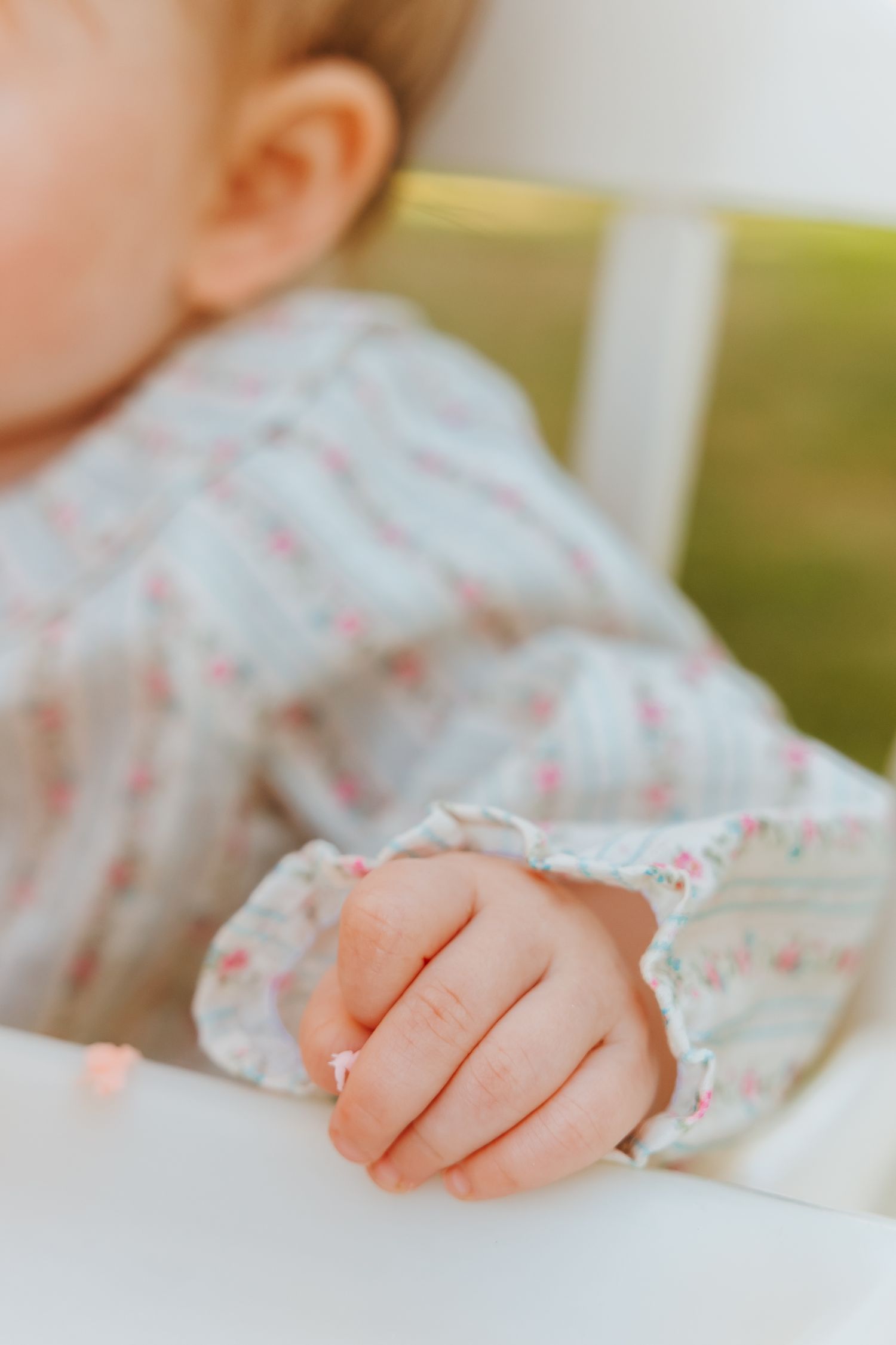 Close-up of a tiny baby's hand resting on white fabric with delicate floral pattern details.